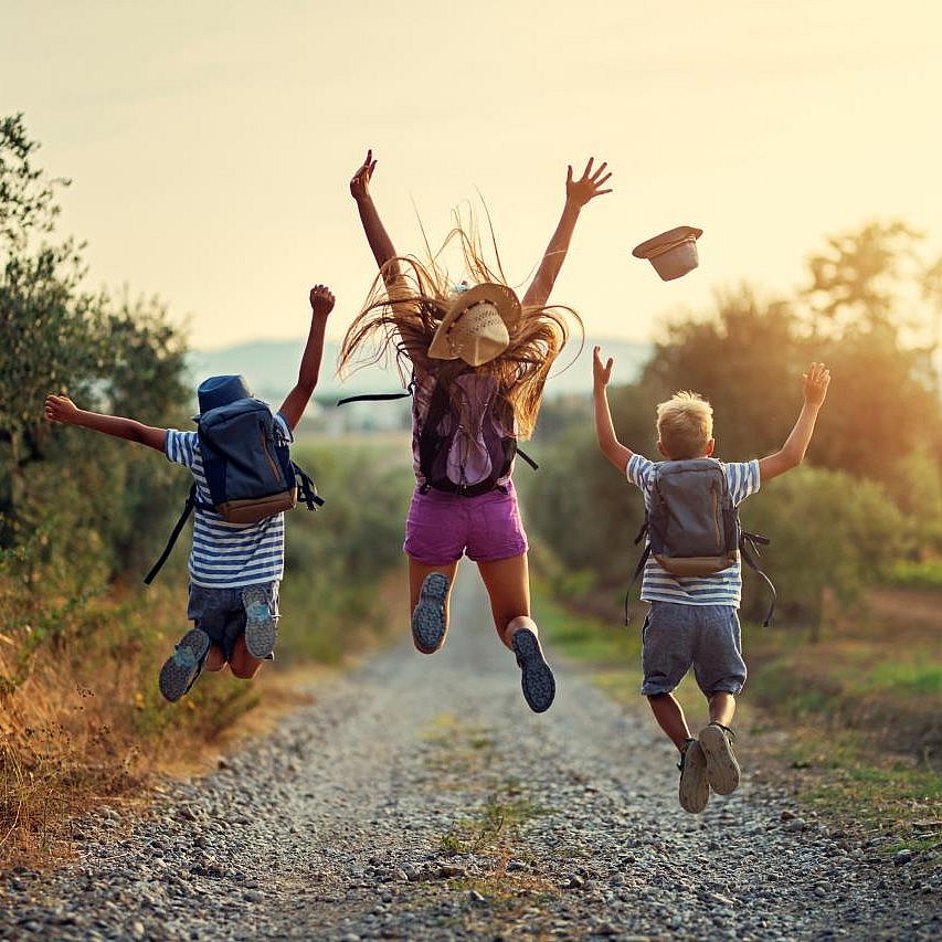Drei Kinder laufen über einen Feldweg und springen vor Freude