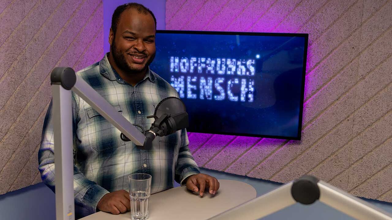 Johannes Schneider steht im Podcaststudio von HOFNNUNGSMENSCH vor einem Mikrofon
