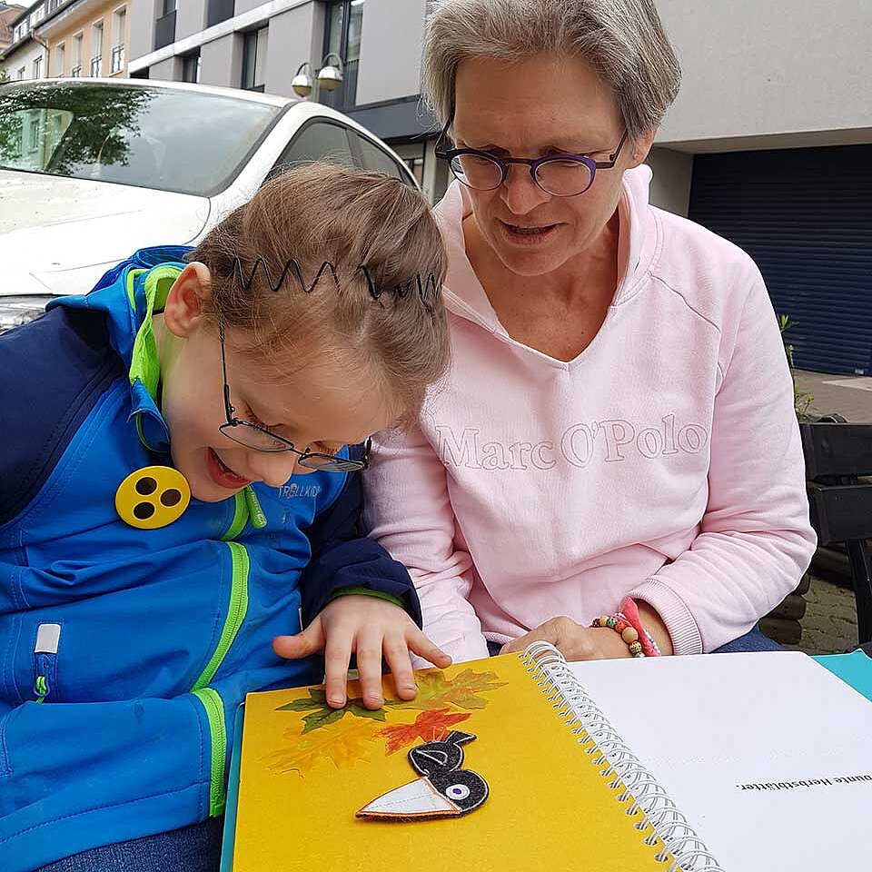 Lukas und Tanja Misof mit einem Fühlbuch in Großdruck: Lukas bringt einen Raben mit Klettverschluss auf der Seite an