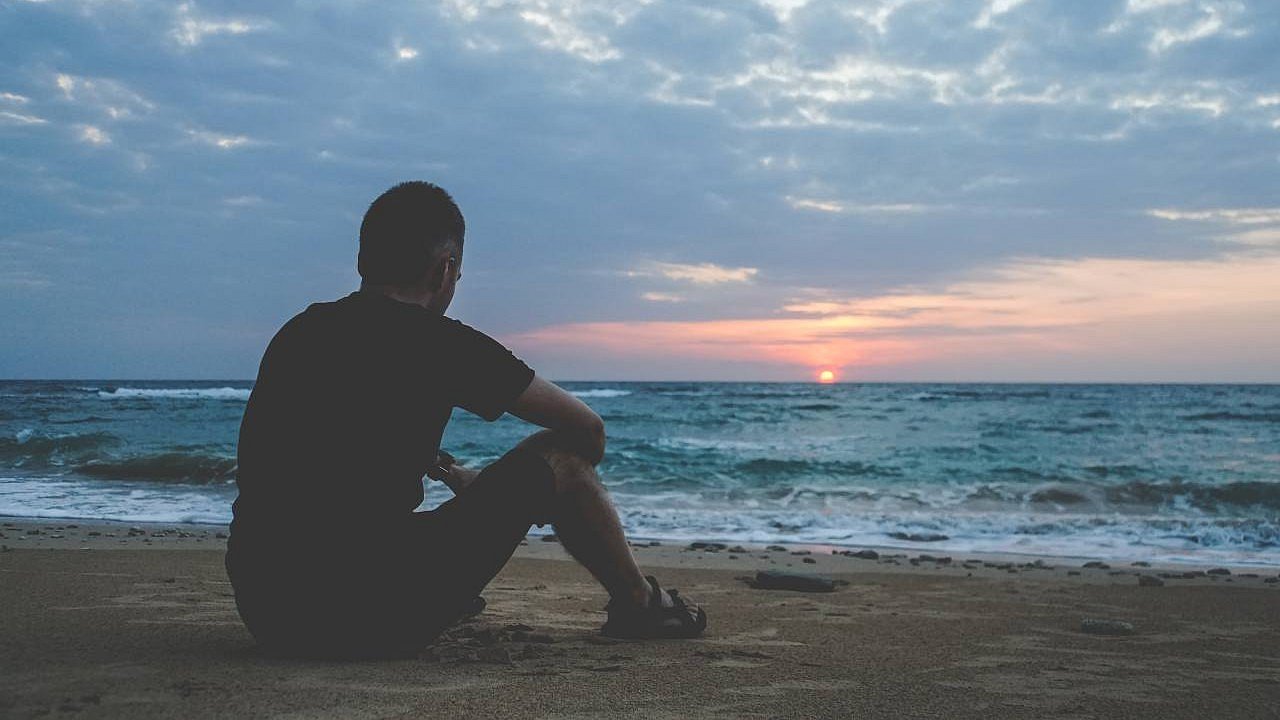 Ein nachdenklicher junger Mann sitzt bei Sonnenaufgang am Meer 
