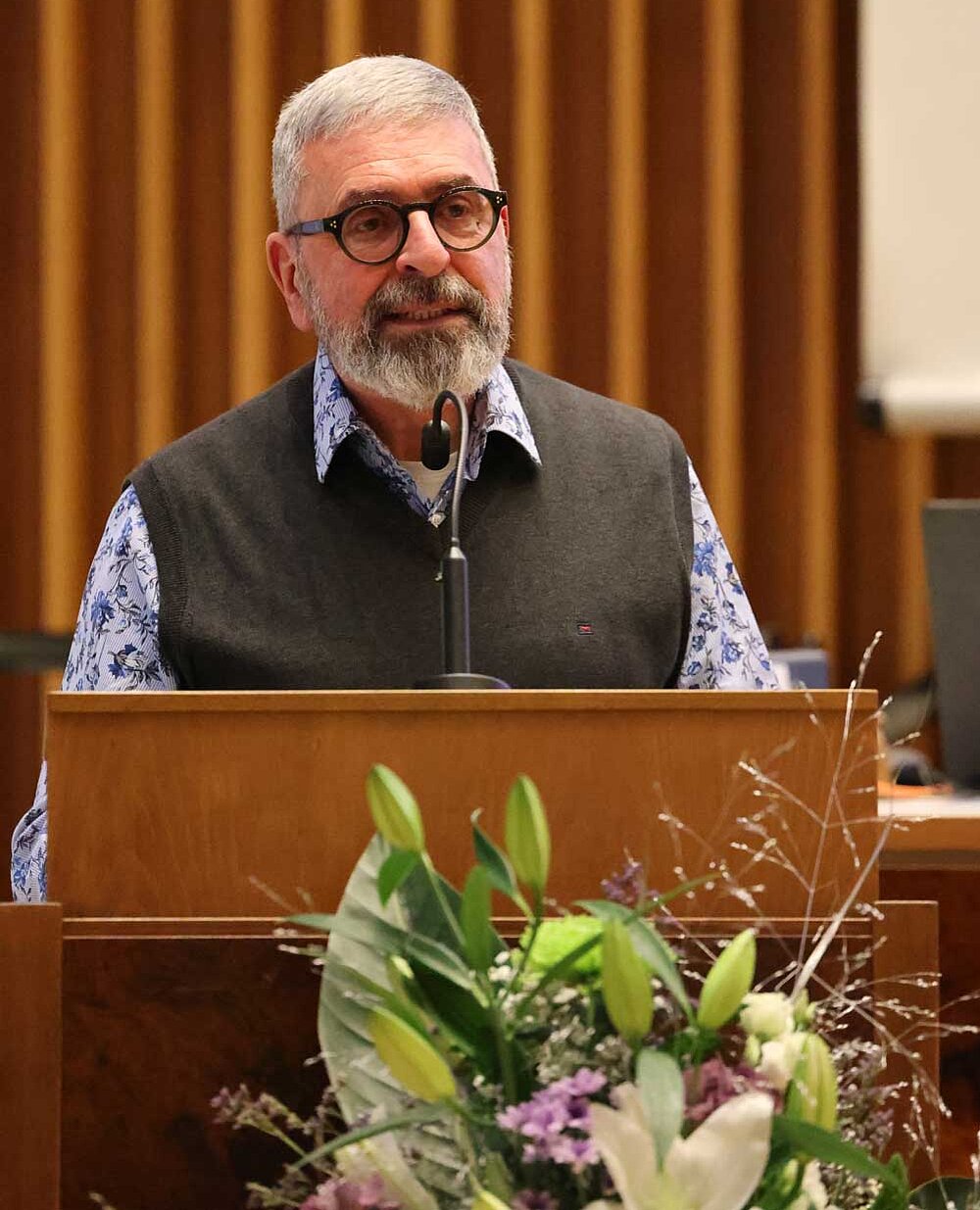 Matthias Schwarz steht am Rednerpult vor der Synode. Im Hintergrund sitzt Petra Knötzele.