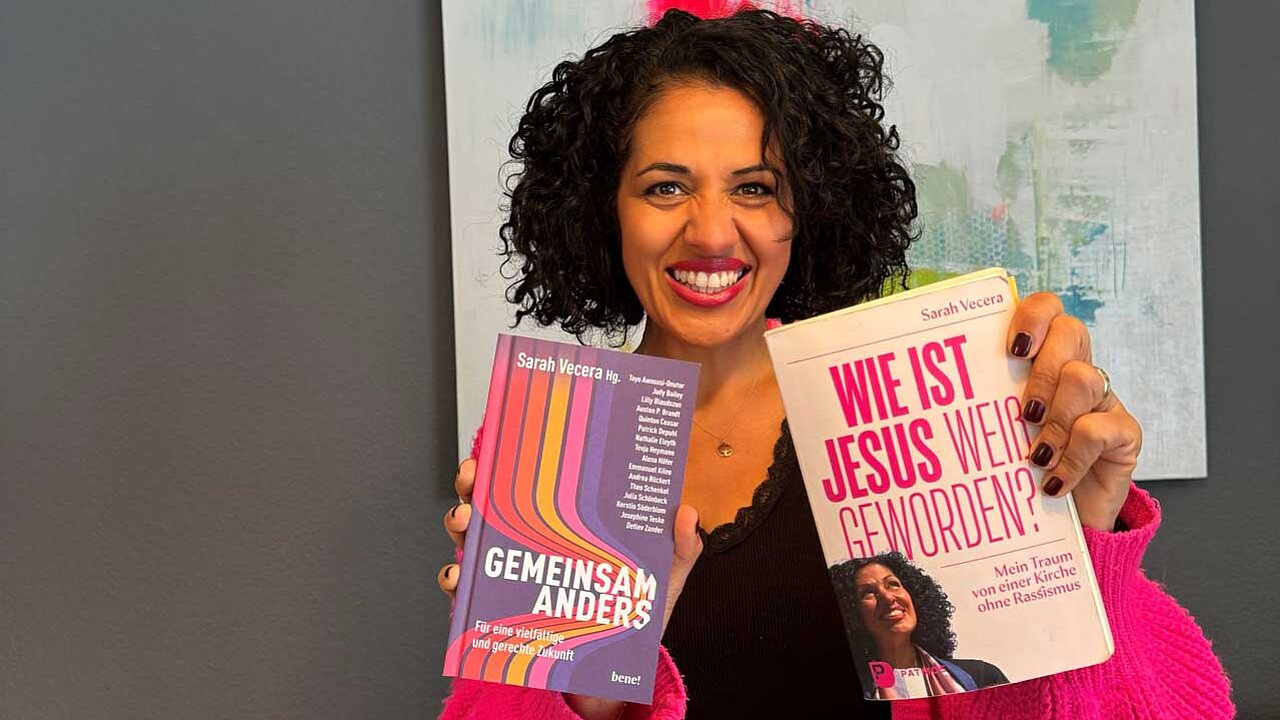 Sarah hält ihre beiden Bücher: „Gemeinsam anders“ und „Wie ist Jesus weiß geworden?“ lächelnd in die Kamera