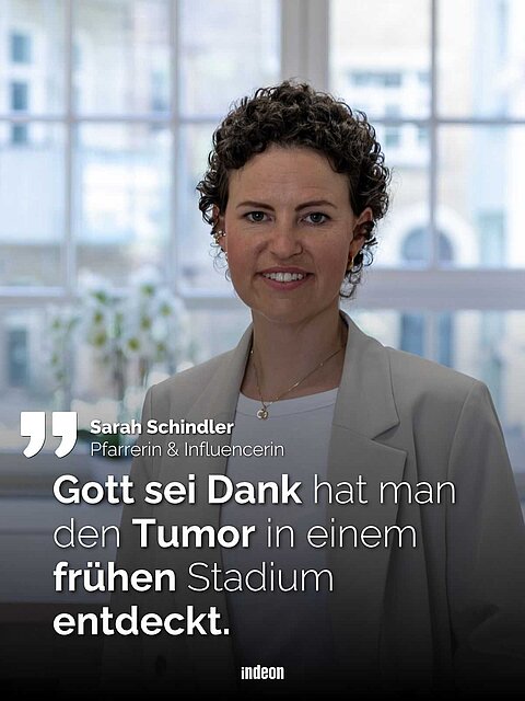 Sarah Schindler. Eine junge Frau, trägt braune, kurze und leicht gelockte Haare. Sie blickt geradeaus und lächelt. Sie trägt einen beigen Blazer