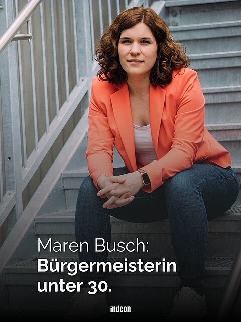 Eine Frau mit brauen Locken und rotem Blazer sitzt auf einer Treppe. Text: Maren Busch. Bürgermeisterin unter 30.