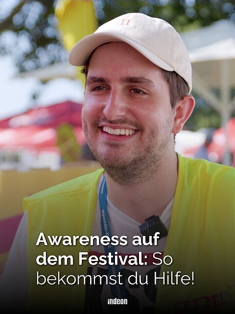 Ein Mann mit gelber Warnweste und weißer Mütze lächelt. Im Hintergrund ein belebtes Musikfestival mit Sonnenschirmen. Text: Awareness auf dem Festival: So bekommst du Hilfe!