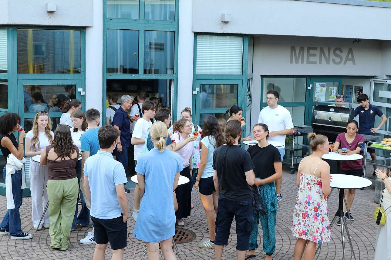 junge Menschen stehen an Tischen, essen und unterhalten sich
