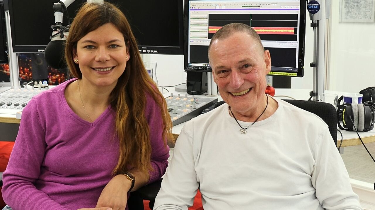 Beide sitzen im Studio und lächeln in die Kamera