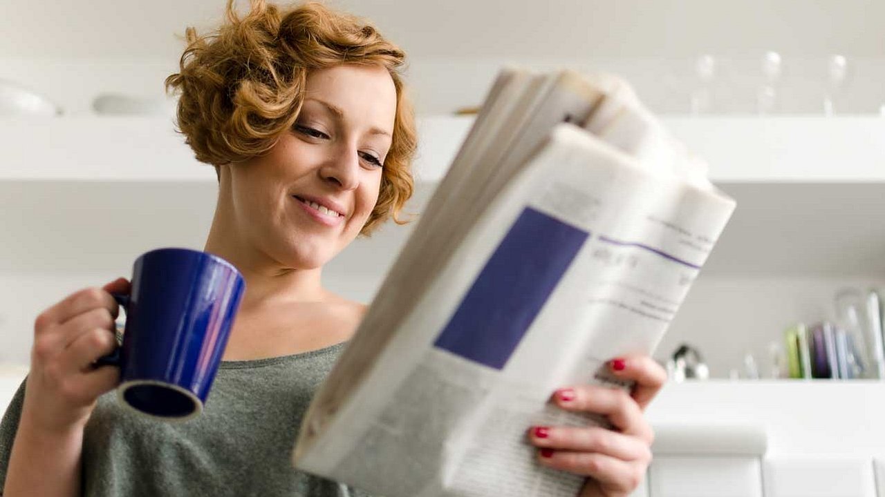 Frau liest Zeitung und hält dabei eine Kaffeetasse