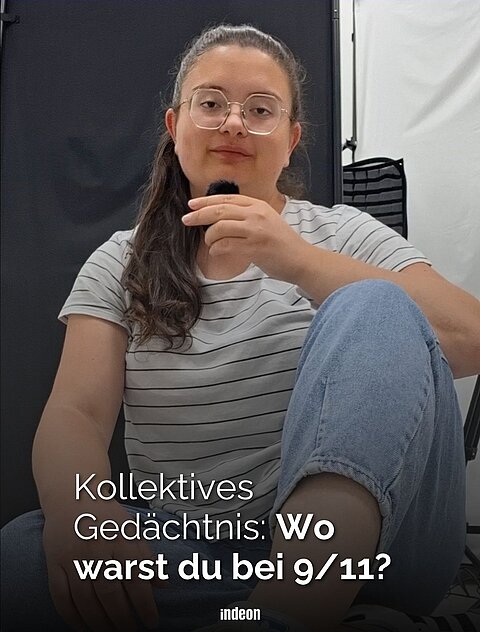Selina von indeon sitzt auf dem Boden und hält ein Mikro in der Hand. Sie schaut ernst in die Kamera. 