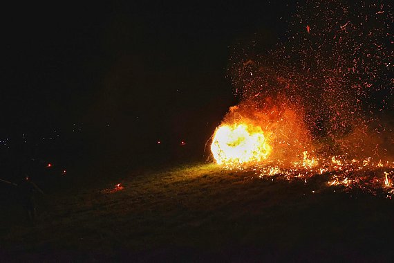 ein brennender Heuballen wird den Berg hinuntergerollt