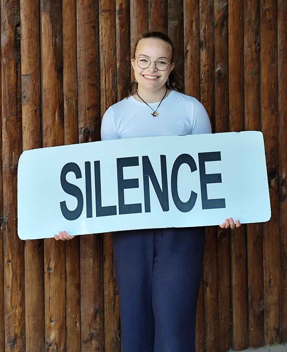 Pauline hält ein Schild mit der Aufschrift „Silence“.