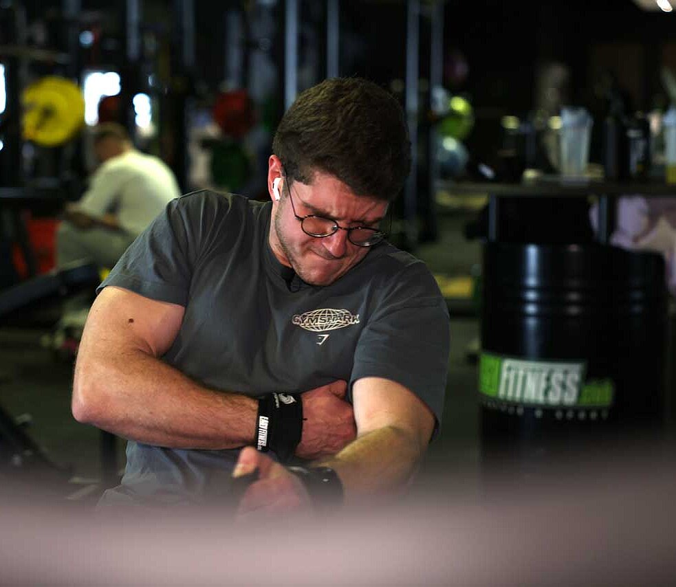Daniel beim Training i Fitnessstudio - er sitzt an einem Gerät, wo er an einer Schnur ziehen muss, an der viel Gewicht dran ist. 