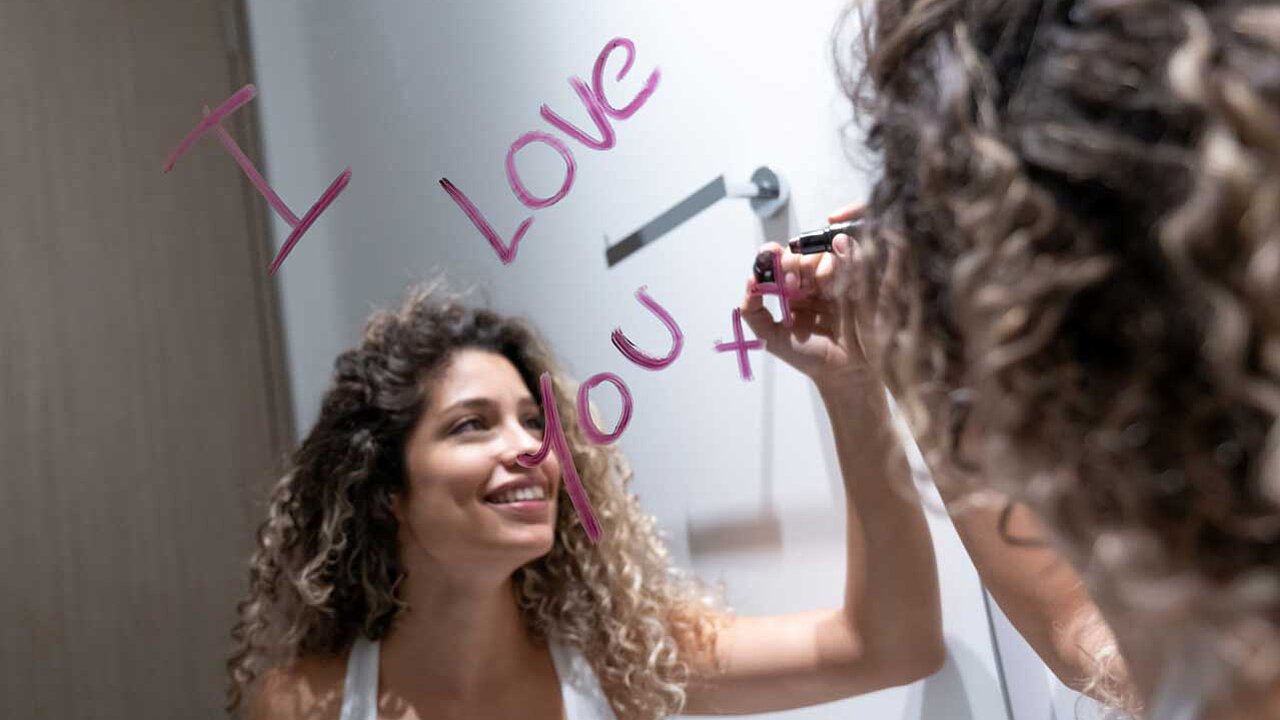 Spiegelbotschaft: I love you - geschrieben von einer jungen lockigen Frau, die unscharf im Spiegelbild zu sehen ist.