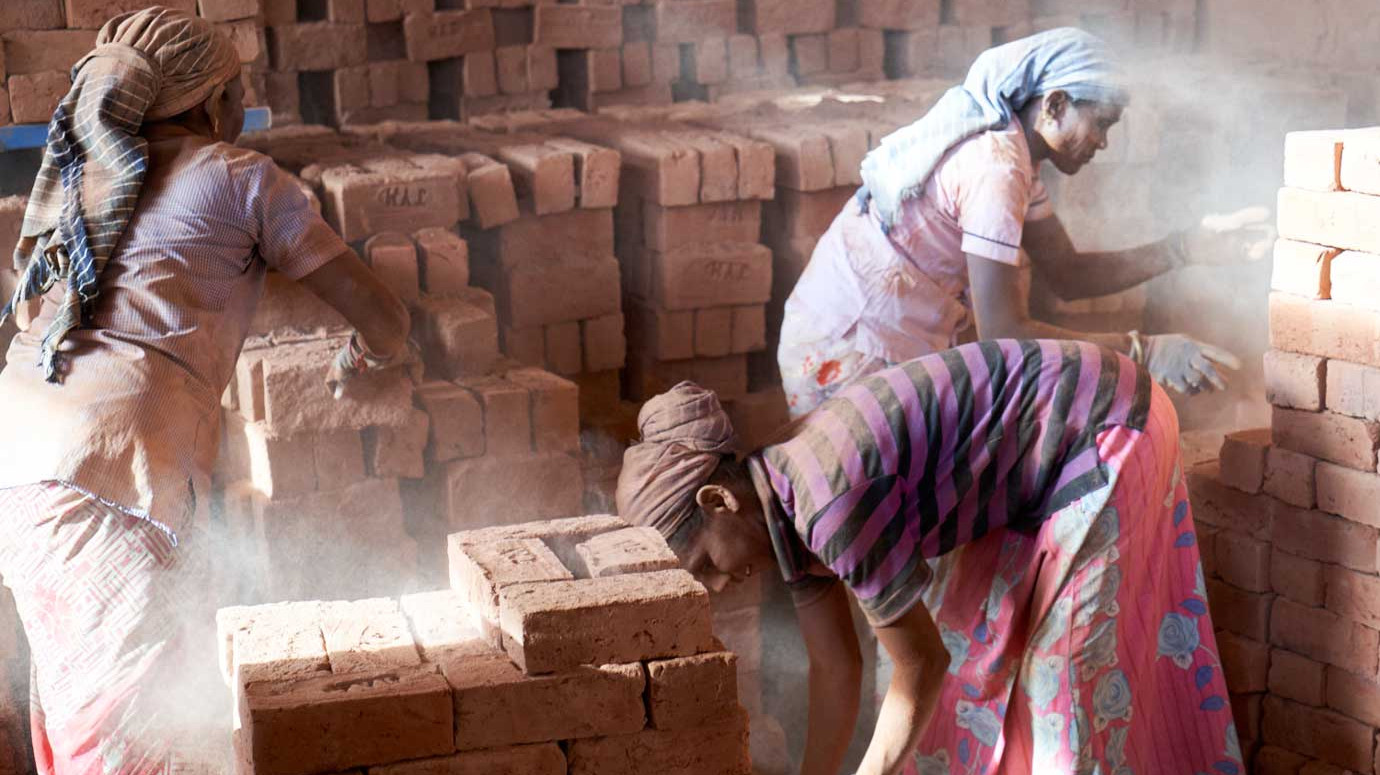 Frauen arbeiten in Ziegelei, viele Ziegelsteine und drei Frauen im Bild mit bunten Kleidern