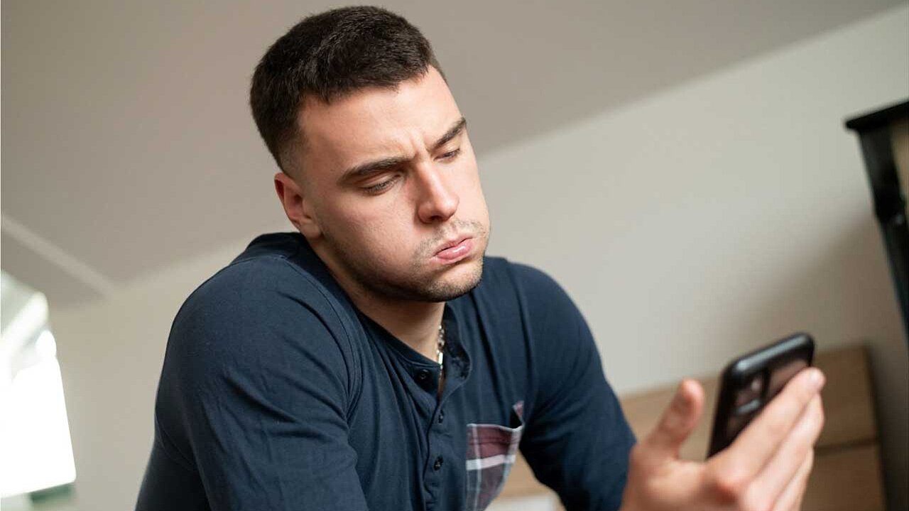 Junger Mann schaut gestresst auf sein Smartphone