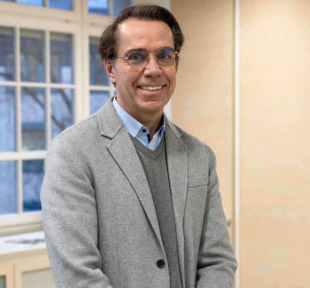 Portrait von Falk Kiefer. Er trägt ein helles Sakko über einem hellbraunen Pullover. Er lächelt freundlich in die Kamera