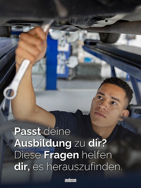 Junger Mann arbeitet mit einem Schraubenschlüssel unter einem Auto in einer Kfz-Werkstatt.