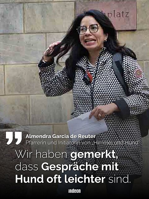 Pfarrerin Almendra García de Reuter mit Brille und gemustertem Mantel läuft mit Papier in der Hand vor einer Steinwand, Zitattext: "Wir haben gemerkt, dass Gespräche mit Hund oft leichter sind."
