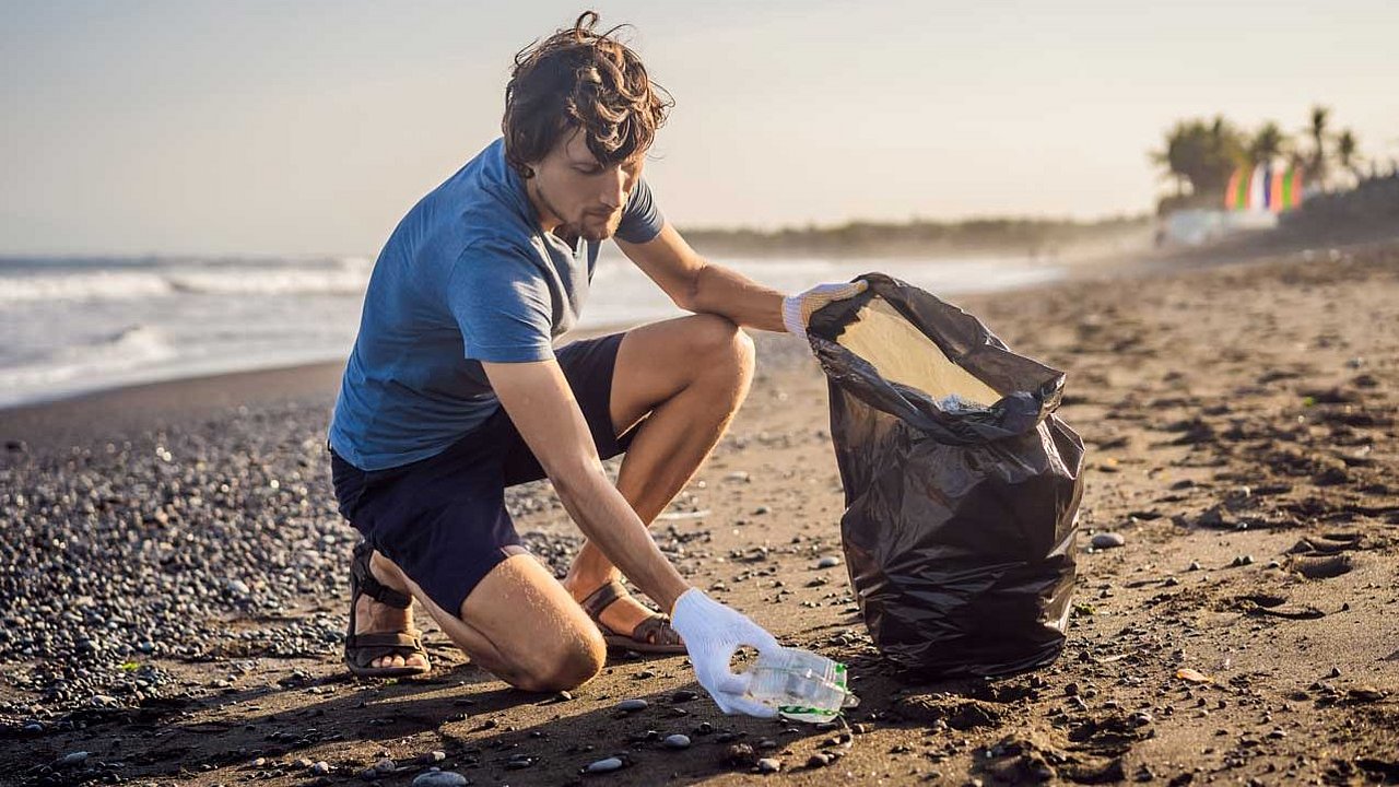 Mann sammelt am Strand Müll in einer Plastiktüte ein 