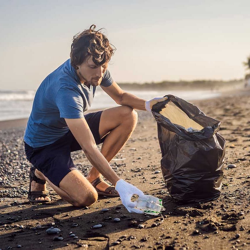 Mann sammelt am Strand Müll in einer Plastiktüte ein 