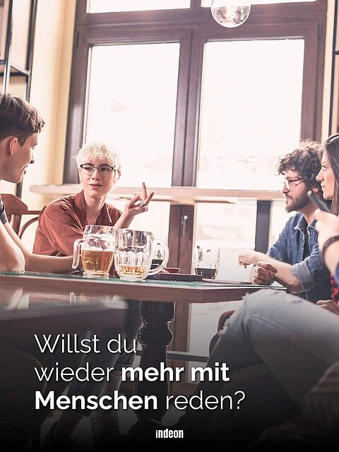 Eine Gruppe von jungen Menschen sitzt um einen Tisch in einer Bar herum. Auf dem Tisch stehen Getränke. Text: Willst du wieder mehr mit Menschen reden?
