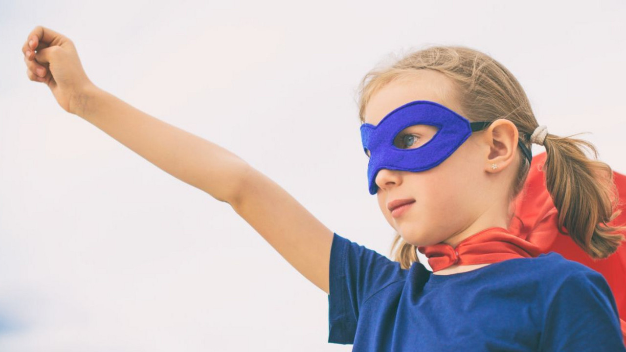 Mädchen im Superheldinnen-Kostüm streckt den Arm nach oben und macht eine Faust