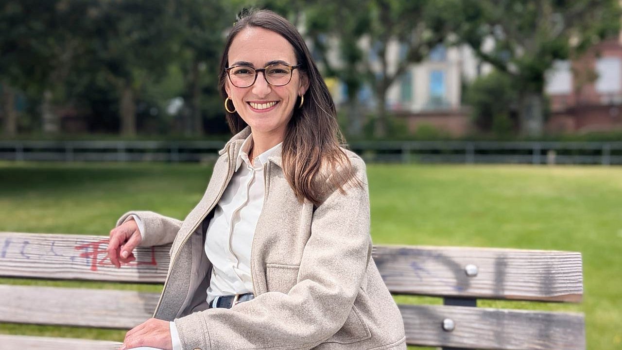 Stephanie Hecke sitzt auf einer Bank und lächelt in die Kamera