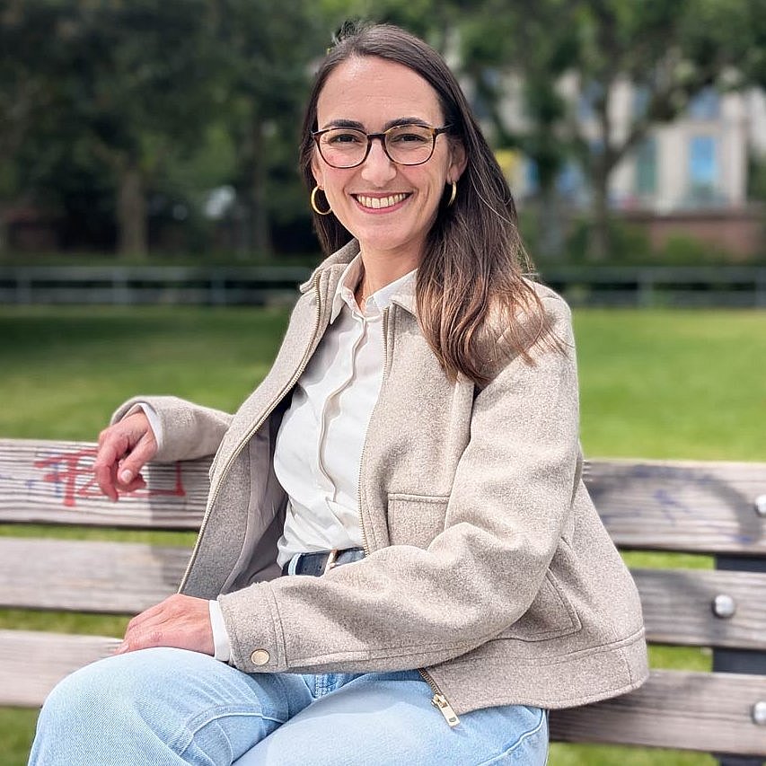Stephanie Hecke sitzt auf einer Bank und lächelt in die Kamera