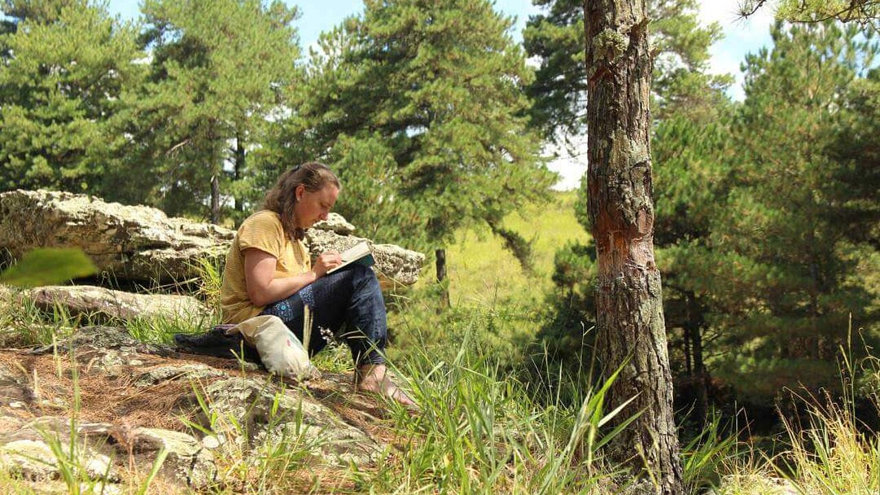 Jasmin sitzt in sommerlicher Landschaft auf einem Felsen.