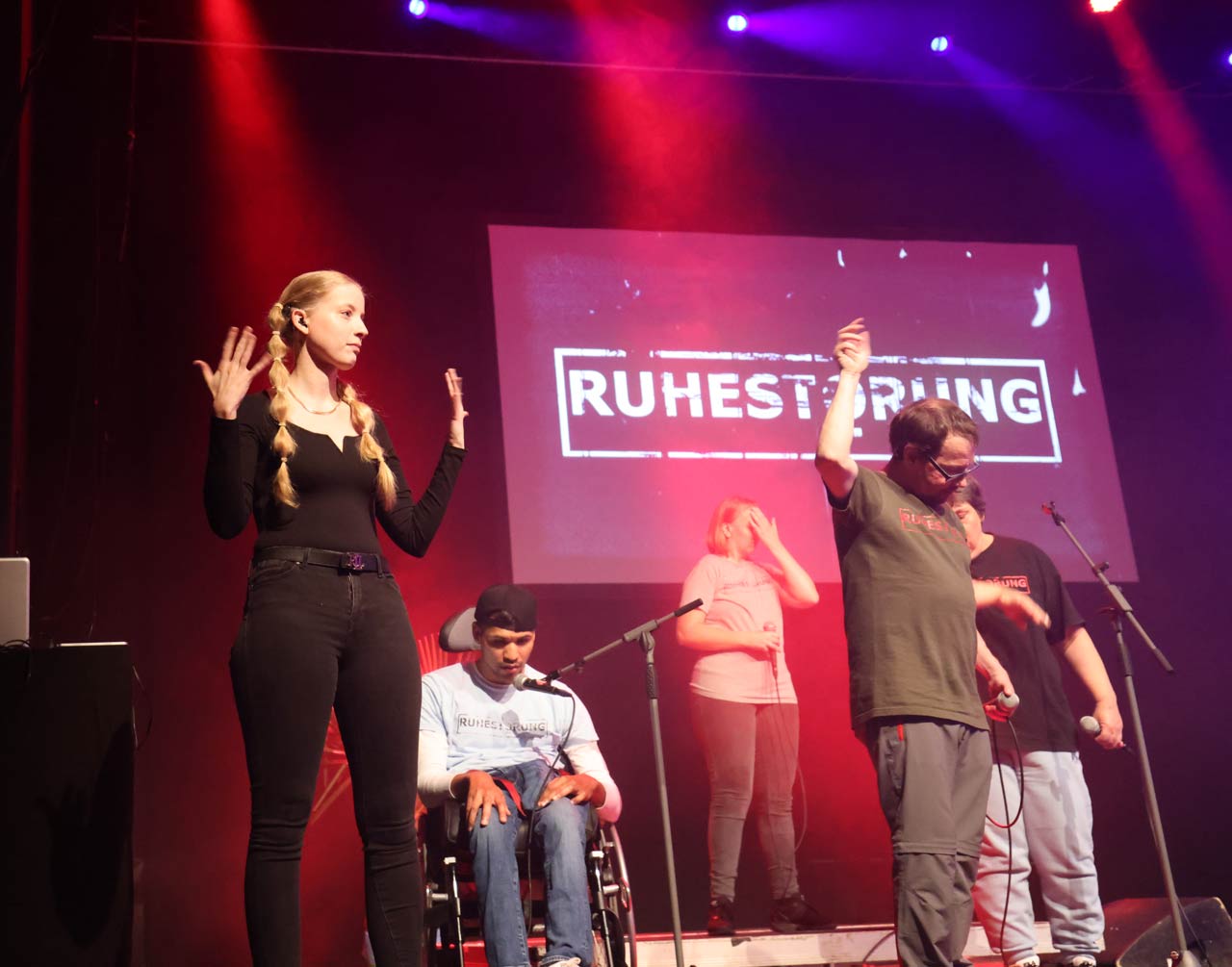 Cindy Klink performt zu den Coversongs der Band Ruhestörung auf der Bühne.  Sie steht links, während rechts die Bandmitglieder singen und tanzen. 