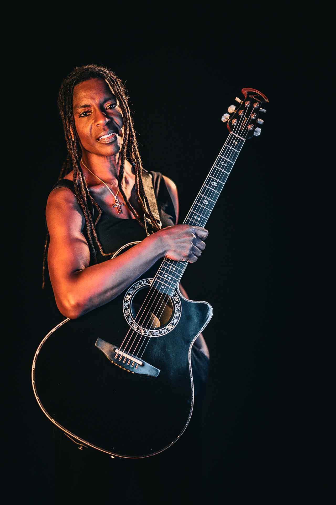 Judy Bailey und ihre Gitarre. Sie steht in einem Foto-Studio und schaut mit starkem Blick in die Kamera. 