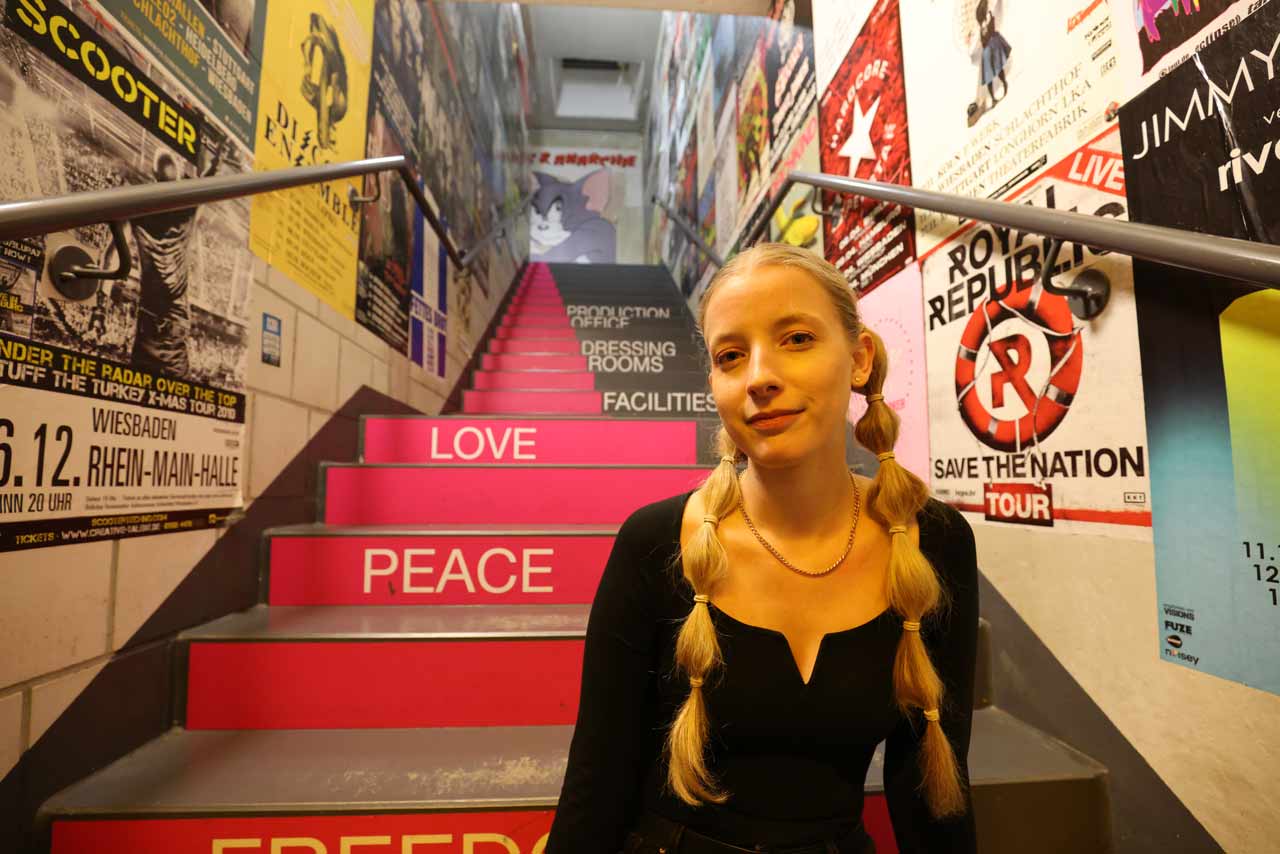 Cindy Klink sitzt auf Treppen im Schlachthof Wiesbaden. Sie hat zwei blonde lange Zöpfe.