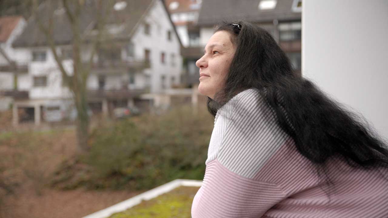 Cornelia steht auf dem Balkon und blickt in ihre neue Nachbarschaft