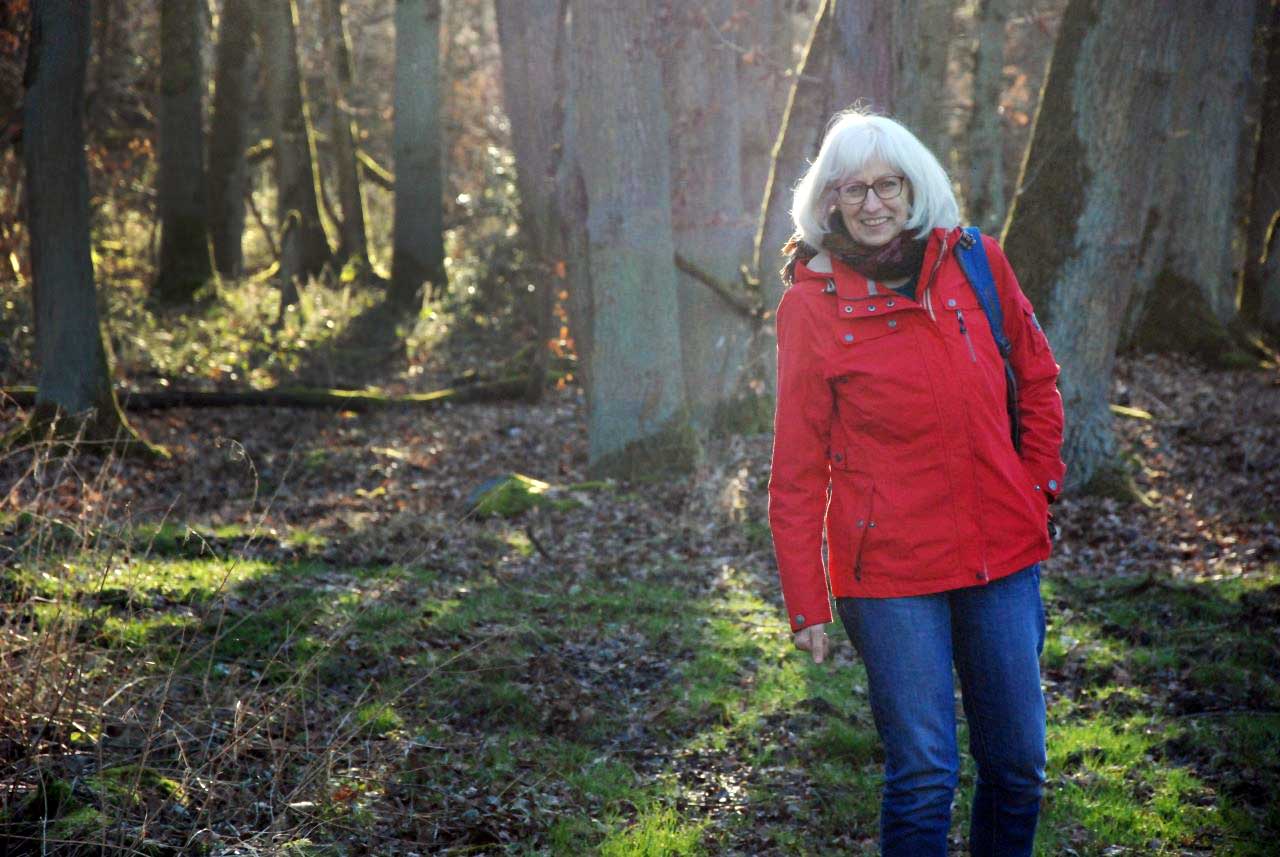 Eine Frau in einer roter Jacke steht in einem Wald.