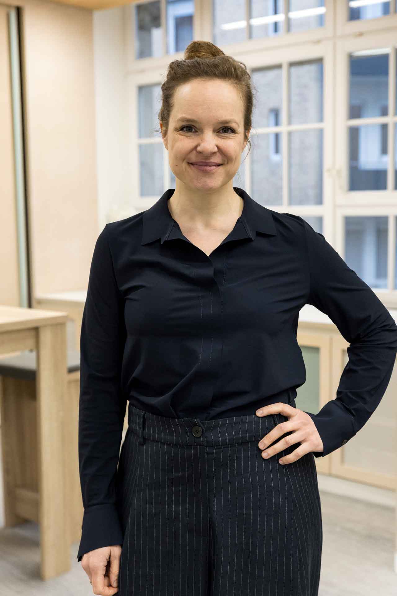 Nathalie Stüben trägt eine schwarze Bluse und eine schwarze Nadelstreifenhose. Sie lächelt freundlich in die Kamera.