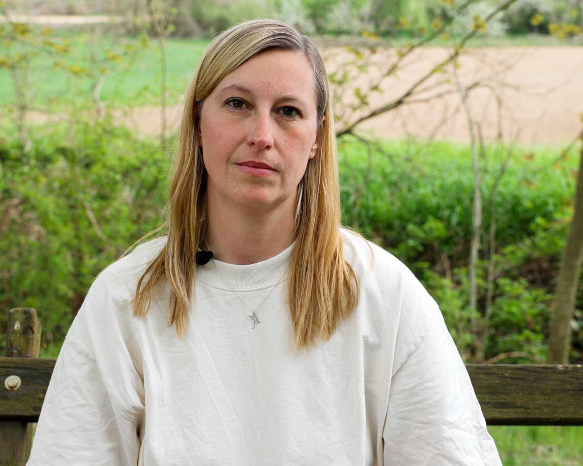 Julia sitzt auf einer Parkbank in den Weinbergen und blickt ernst in die Kamera