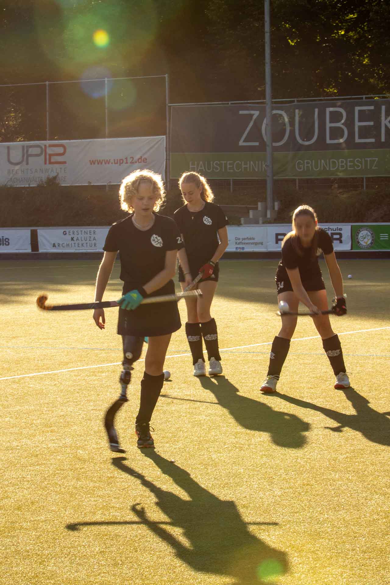 3 Mädchen mit Hockeyschlägern auf dem Feld