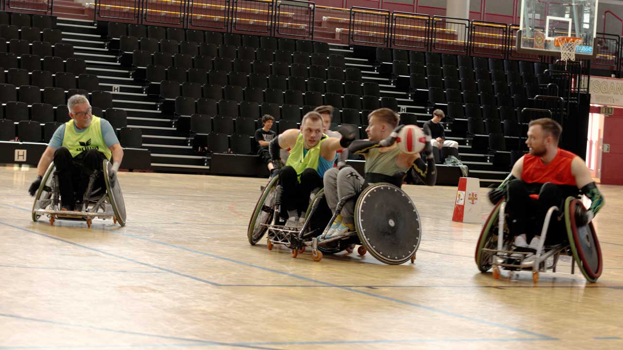 Florian spielt Rollstuhlrugby. erträgt dabei ein Neongelbes Leibchen und greift konzentriert nach dem Ball. 