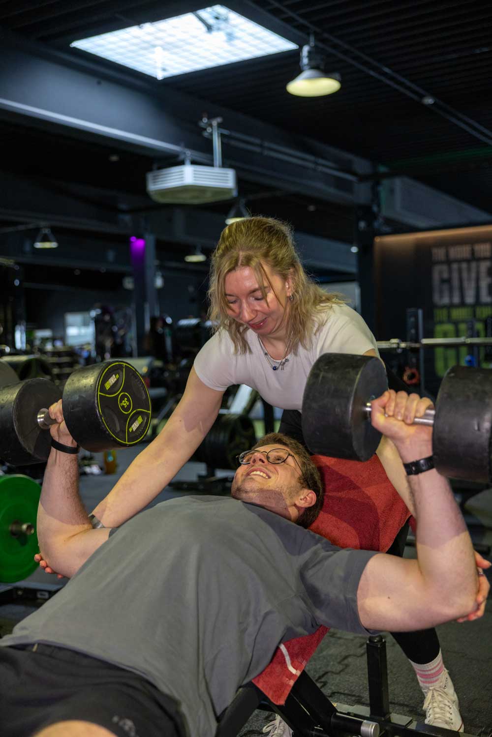 Tabea unterstützt Daniel beim Hanteltraining. Er liegt auf der Hantelbank und hat rechts und links je 35 Kilo in der Hand. Sie hilft ihm dabei, die Übungen sauber auszuführen.