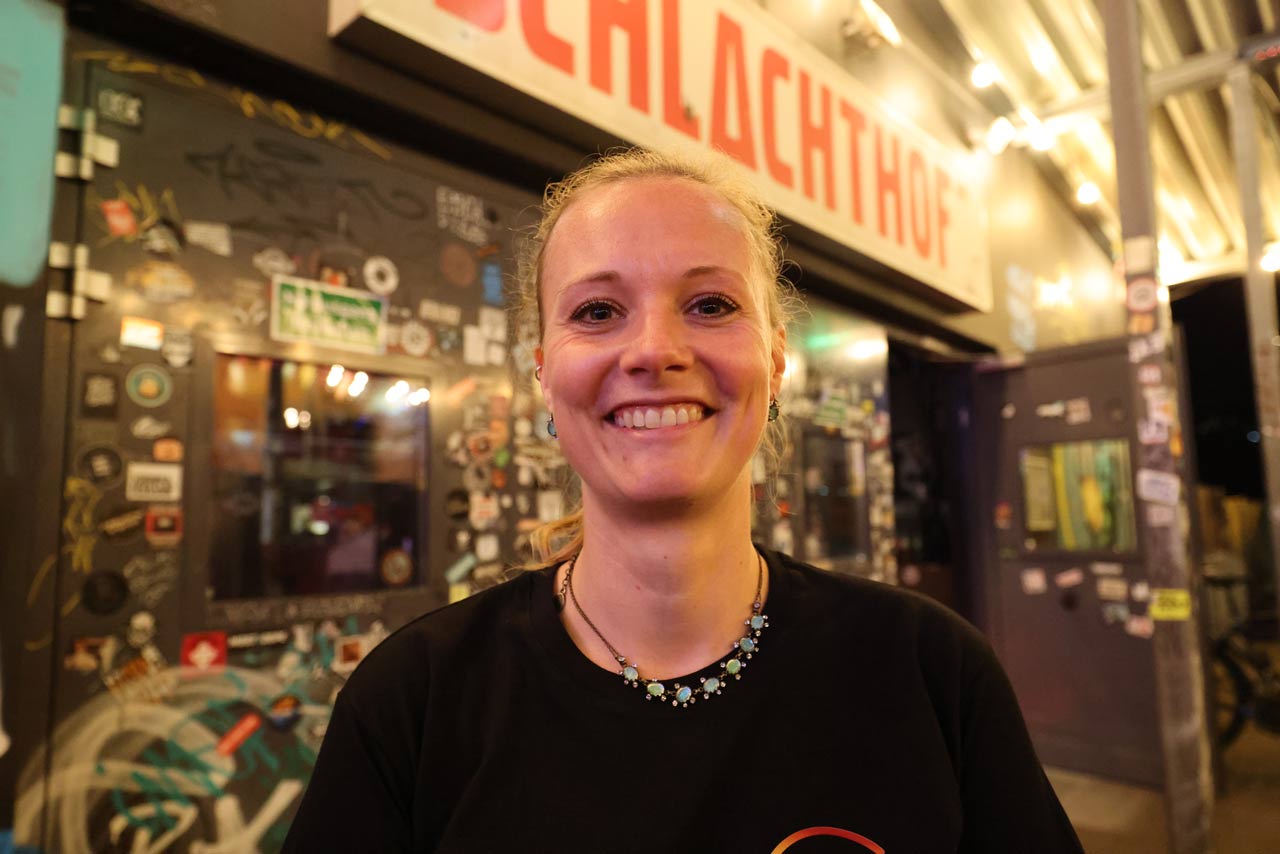 Johanna Schröter arbeitet seit 12 Jahren für EVIM und hat die Party im Schlachthof mit organisiert.  Sie lacht in die Kamera und im Hintergrund sieht man den Eingang des Schlachthofes.