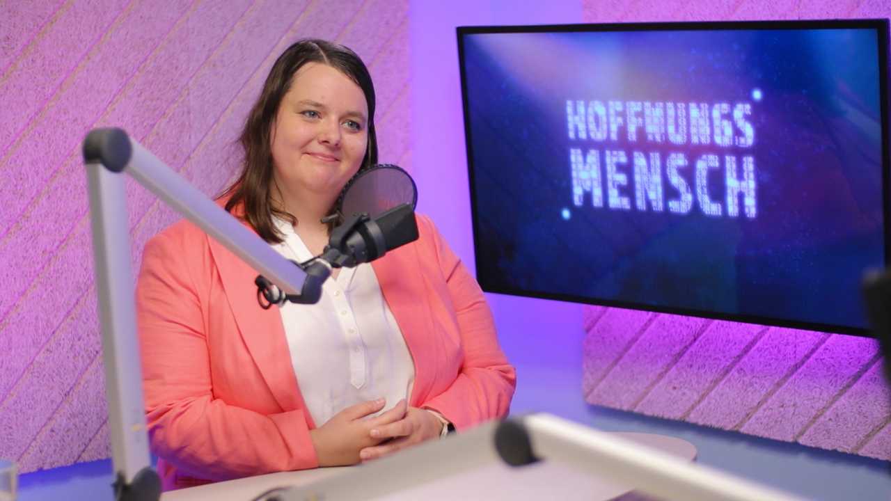 Die Politikerin Lea Blattner trägt einen korallenfarbenen Blazer und eine weiße Bluse. Die 31-Jährige hat schulterlange braune Haare und steht im Studio des Podcasts Hoffnungsmensch.