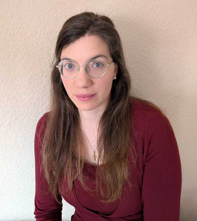 Portrait von Ulrike. Sie blickt gerade in die Kamera, ihre langen braunen Haare fallen über beide Schultern. 