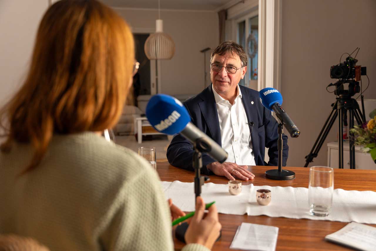 Kirchenpräsident Volker Jung sitzt am Tisch mit einem Mikrofon vor sich. Er nimmt gemeinsam mit Lotte den indeon-Podcast „echt gefragt - der Deeptalk“ auf.