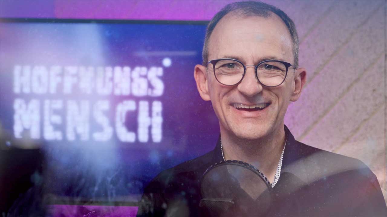 Steffen vorm Mikro. Im Hintergrund das Logo vom Podcast. 