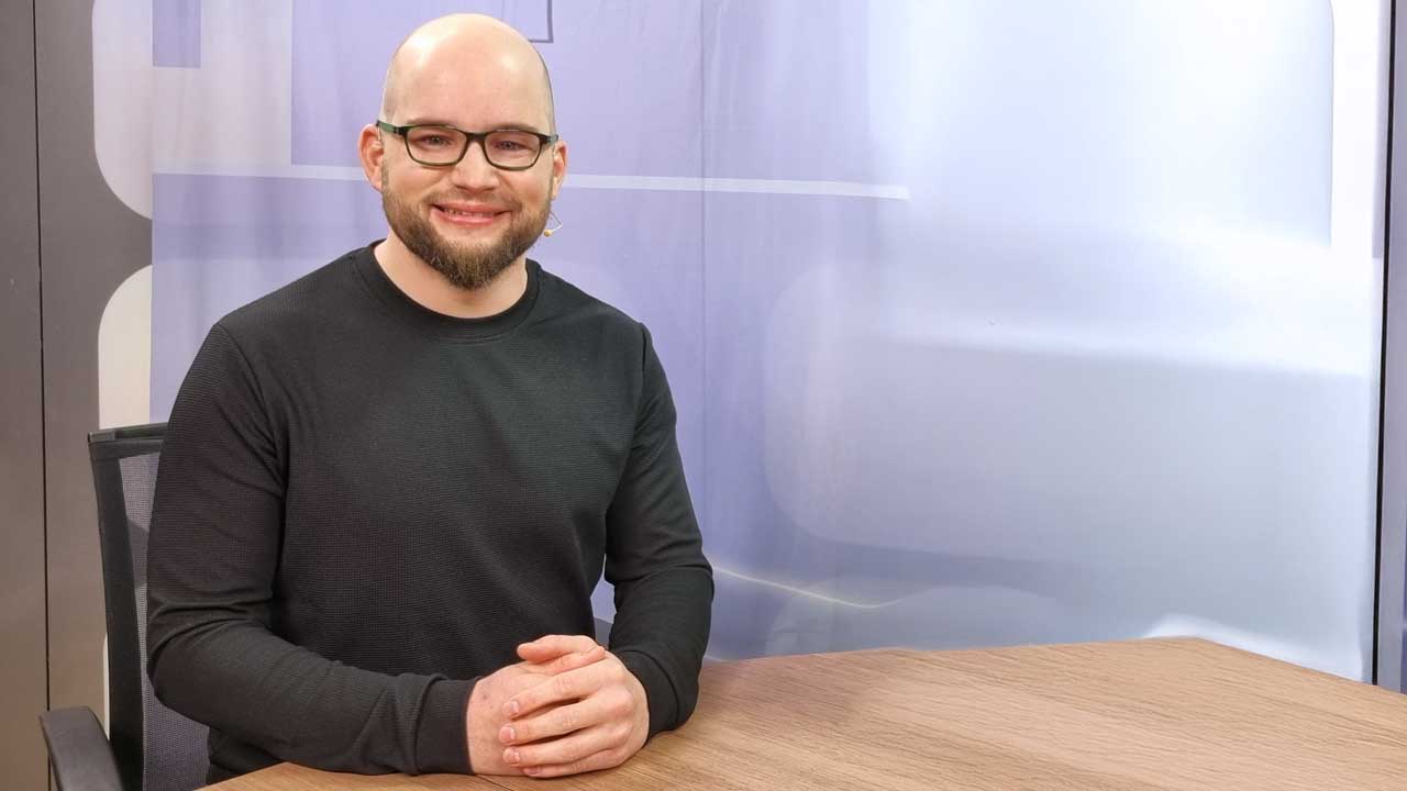 Micha sitzt im Studio von Alpha & Omega und lächelt in die Kamera. 