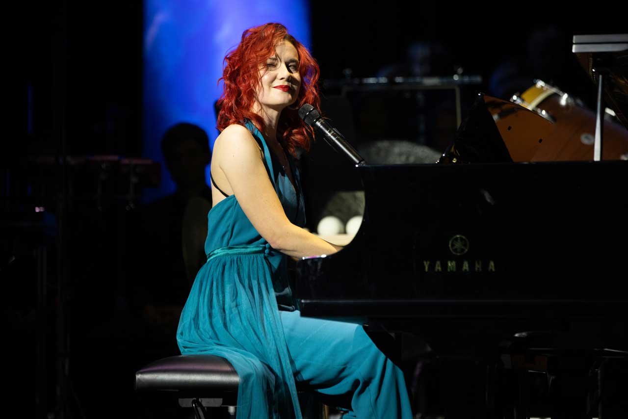 Sarah sitzt auf einer Bühne am Klavier