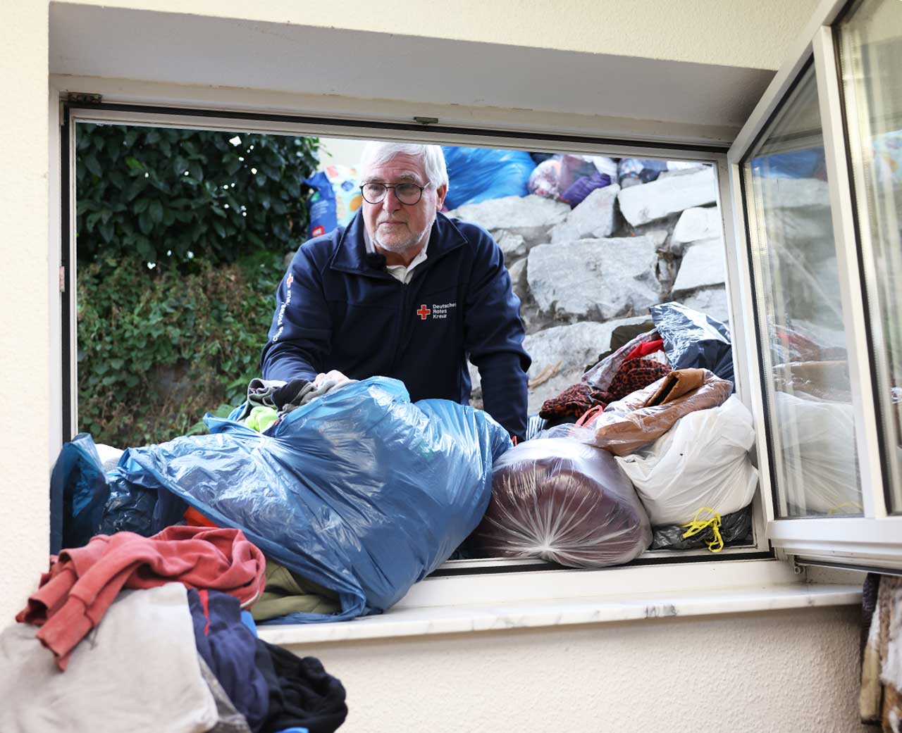 Karlheinz Weinert steht vor dem offenen Fenster. Um ihn herum sind Säcke voller Altkleider,.
