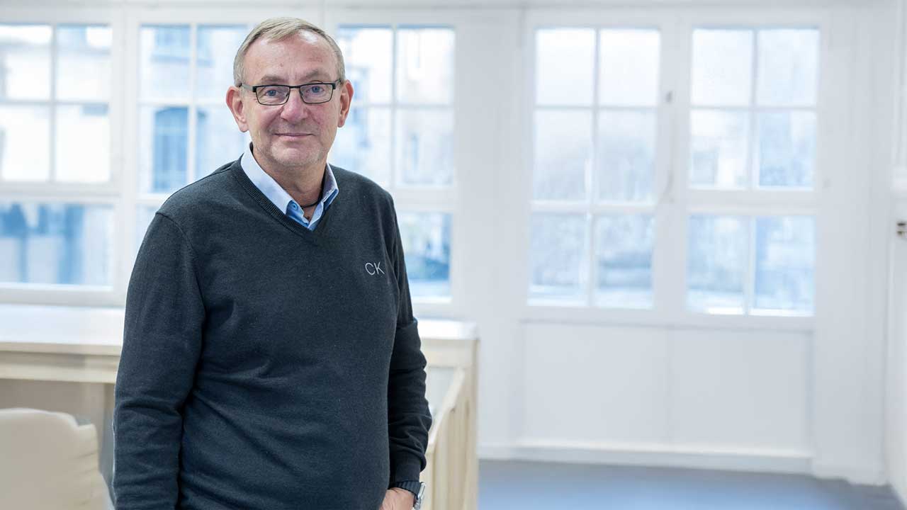 Bernd Siggelow steht in einem hellen Raum und lächelt in die Kamera.