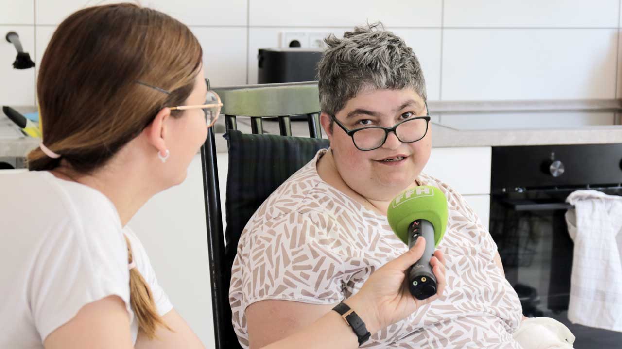 Lotte im Interview mit Vera im Gemeinschaftsraum. Lotte hält ein FFH-Mikrofon. 