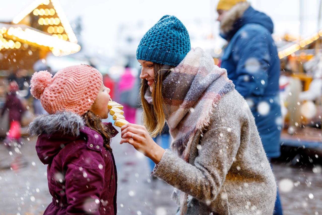 Eine Frau gibt einem Mädchen auf einem Weihnachtsmarkt eine Süßigkeit.